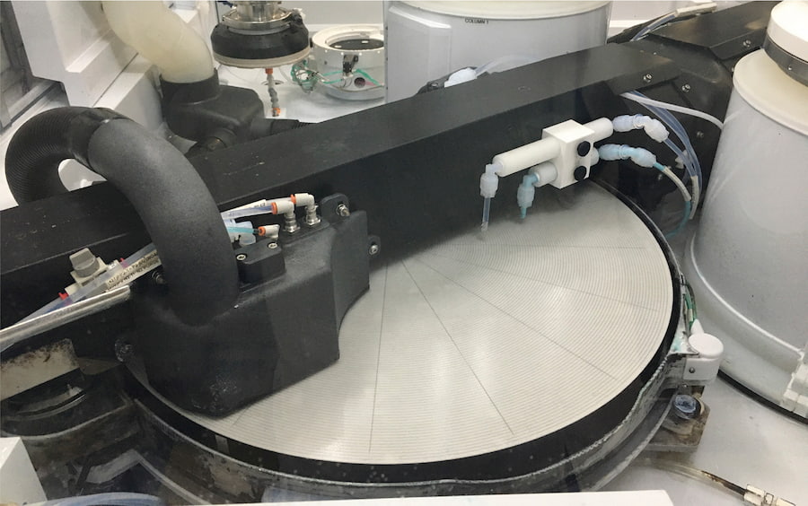 A slurry polishing machine in action, shaping a circular object with precision in a production environment.